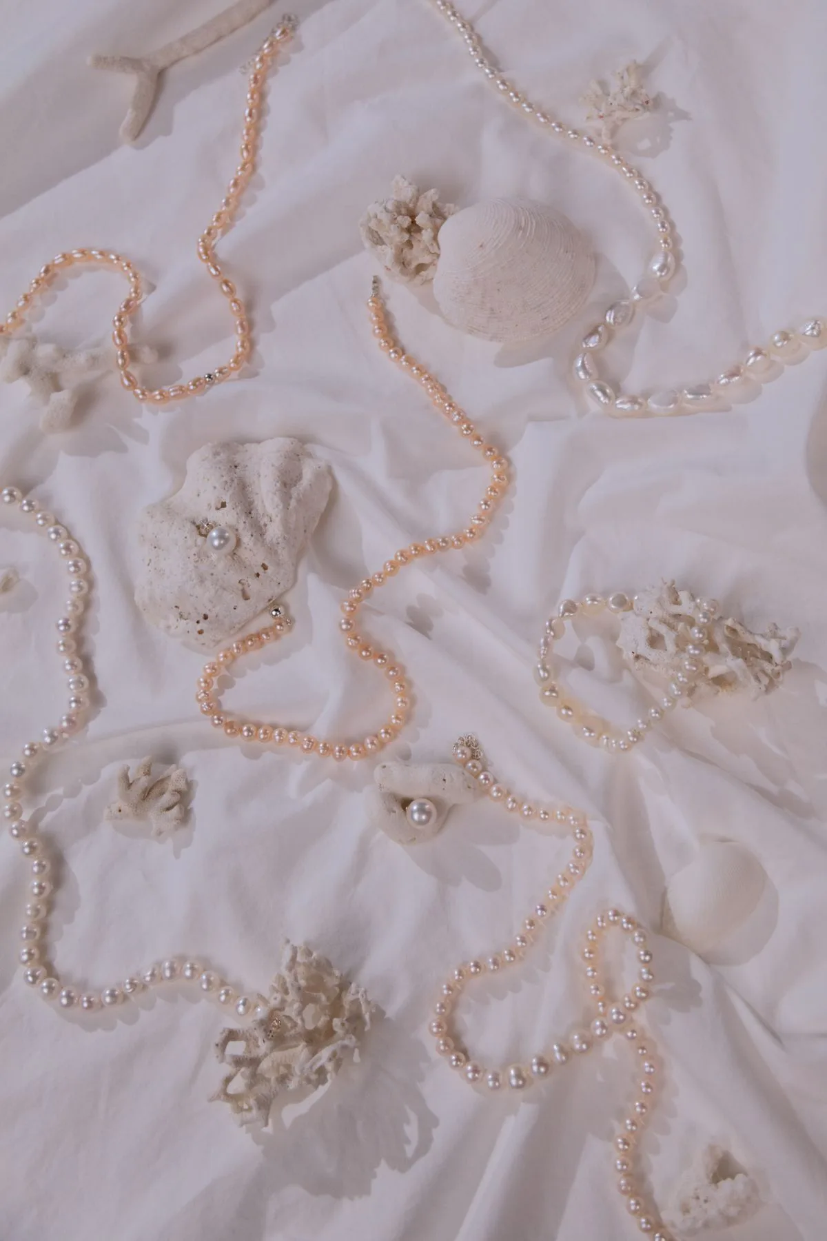 Layered pearl necklaces arranged on soft white fabric with natural shell accents