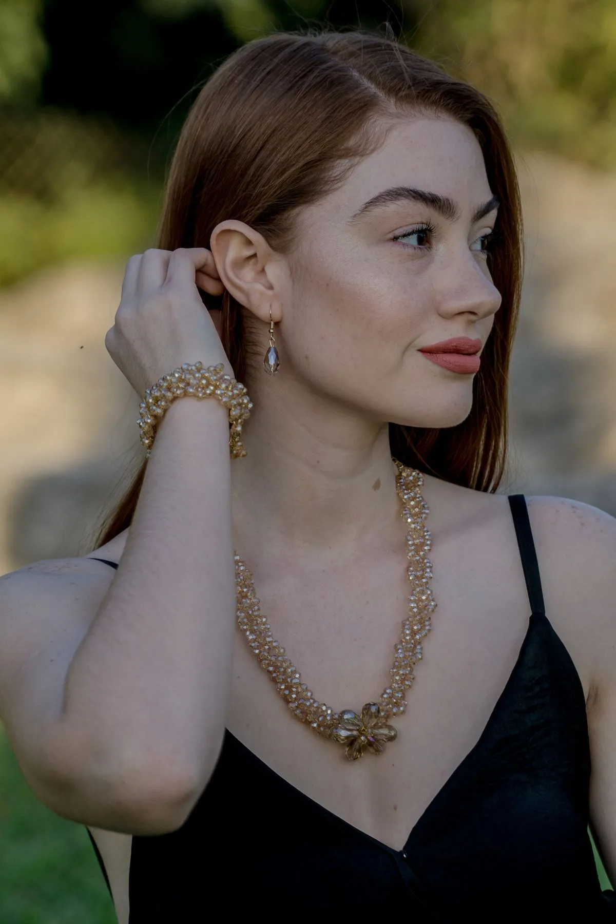 Model wearing a champagne beaded gemstone necklace, bracelet and drop earrings in warm natural light