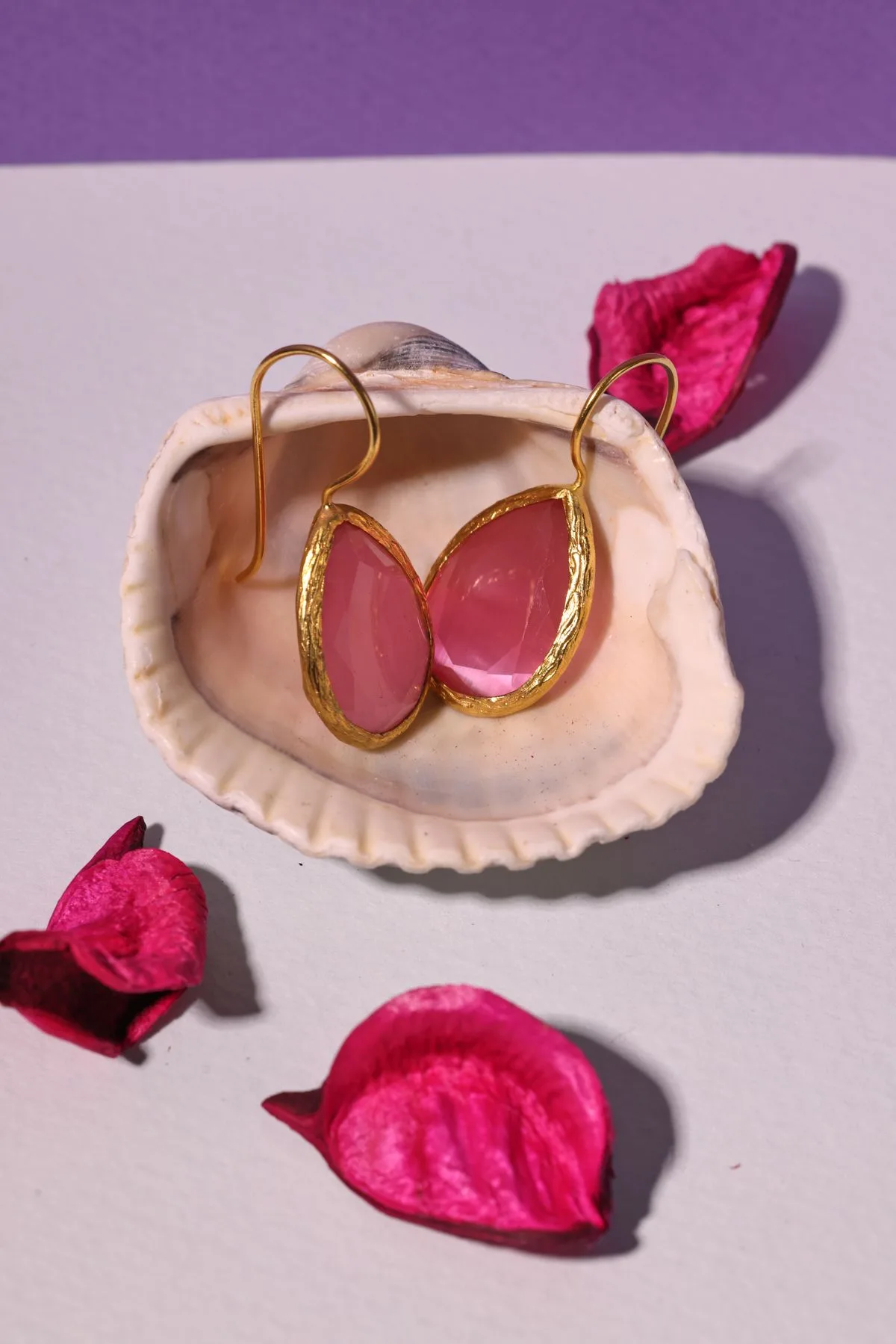 Handmade rose quartz drop earrings nestled in a seashell with flower petals