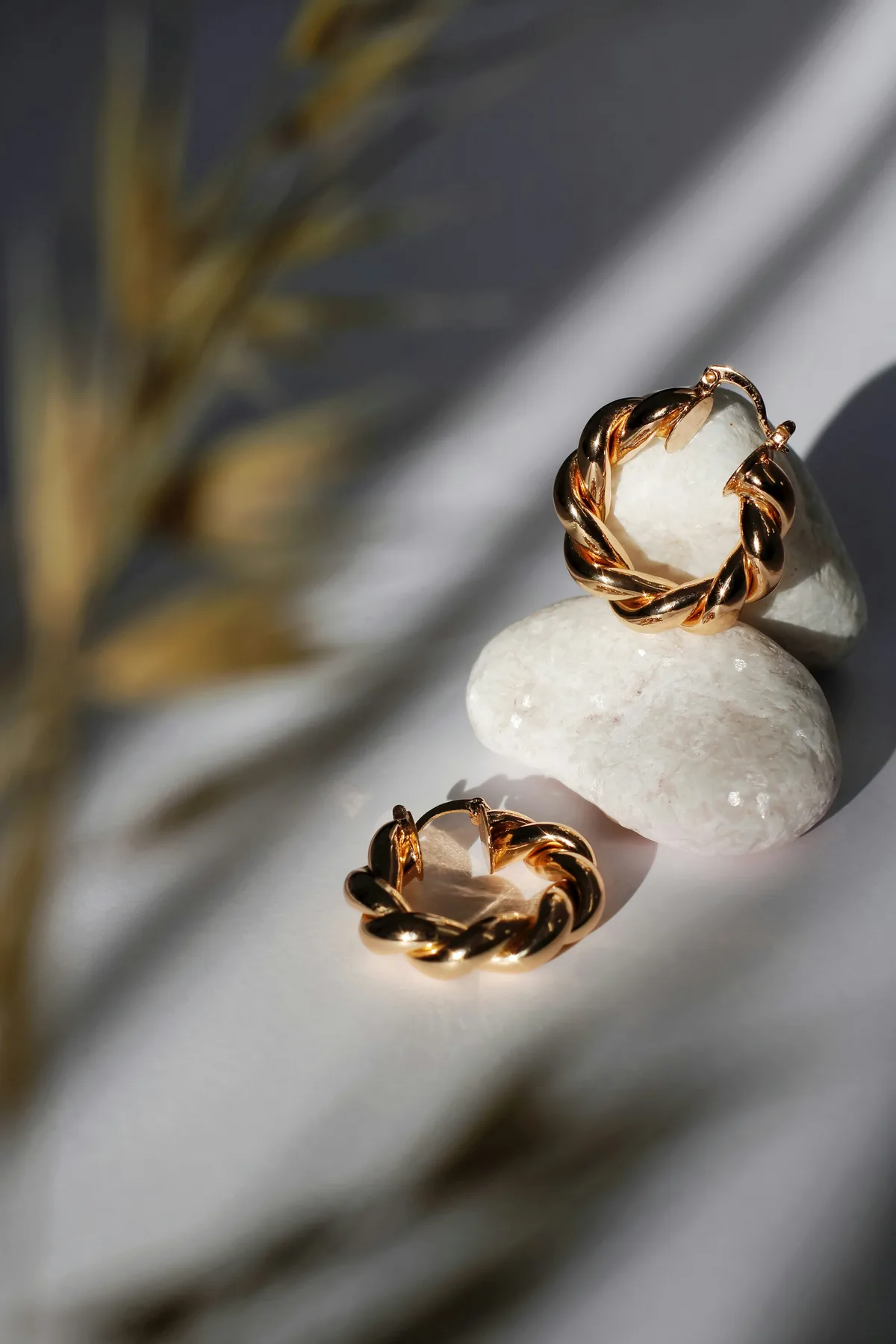 Twisted fashion hoop earrings styled with smooth white stones on a cream surface